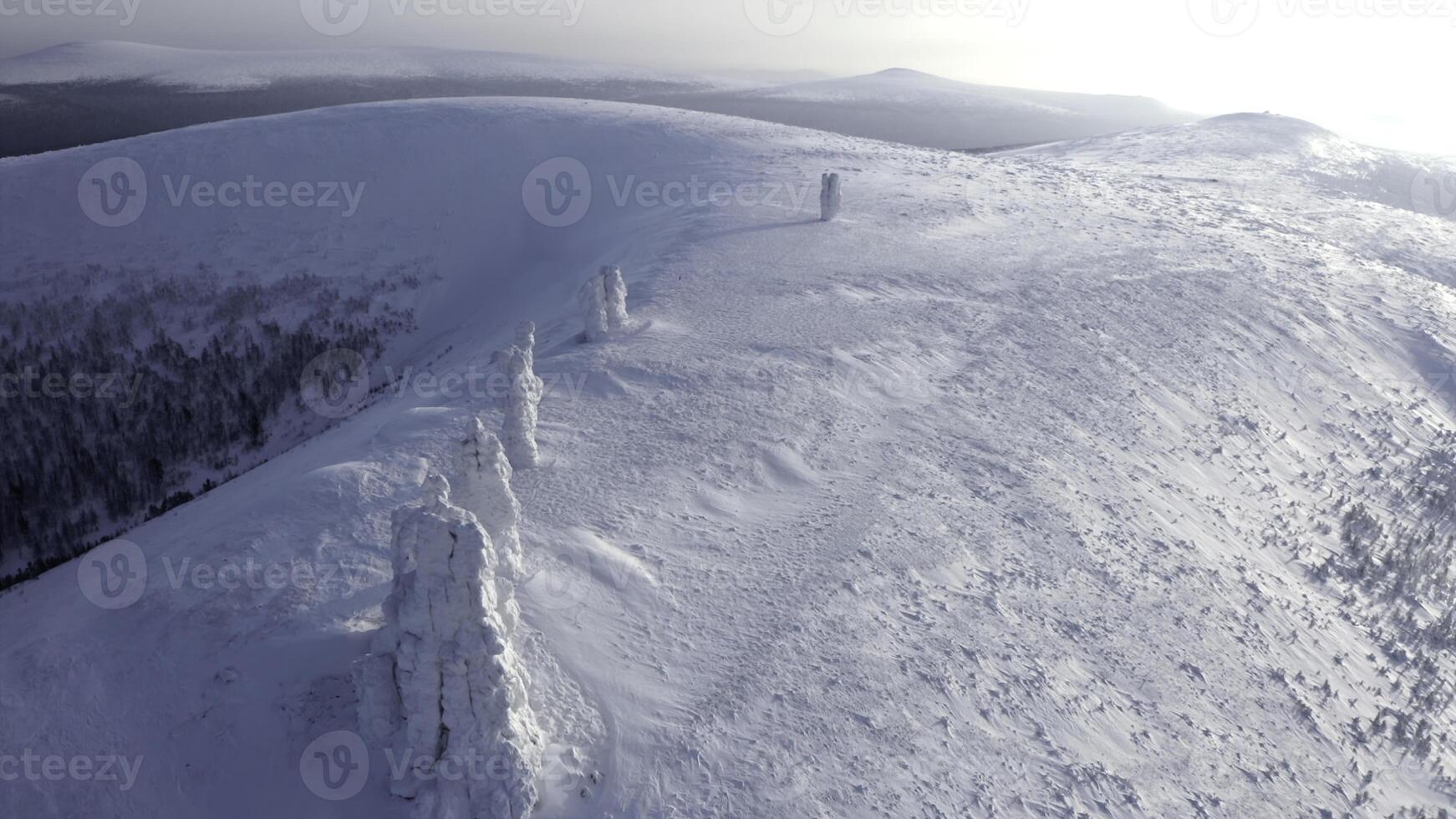 Landscape in sub-zero temperatures from above. Clip.Snowy empty mountains with frozen hills and trees are visible against a bright sky. photo