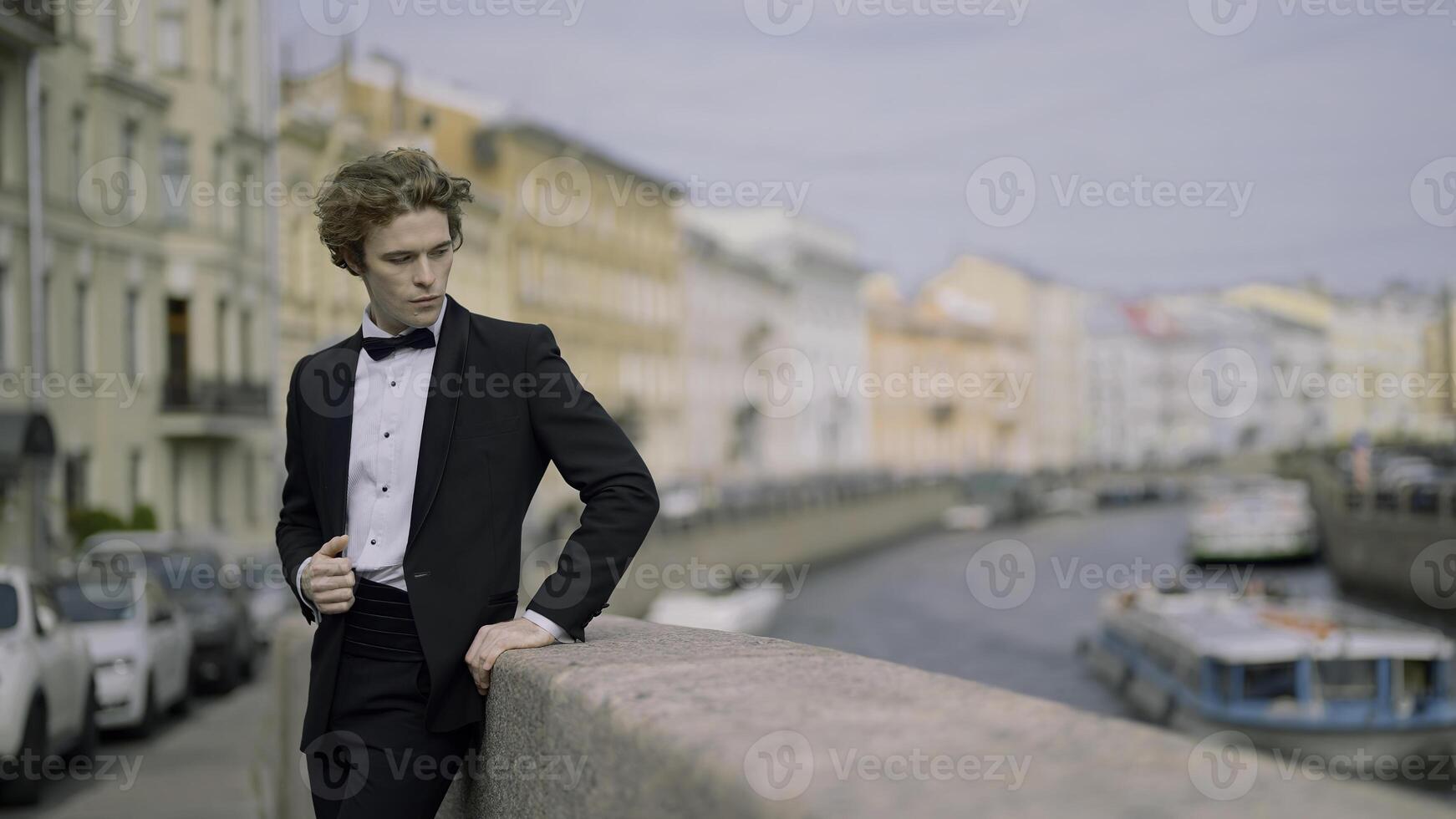 Models posing on the embankment . Action . A handsome, spectacular man in a suit with a bow tie and long hair standing with a young bride and posing for the camera. photo