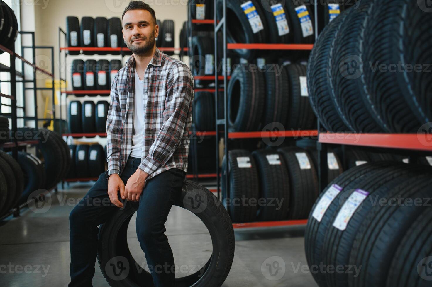 Smart customer taking new tires in the supermarket for buying. He looks happy. Big shopping mall with car goods photo