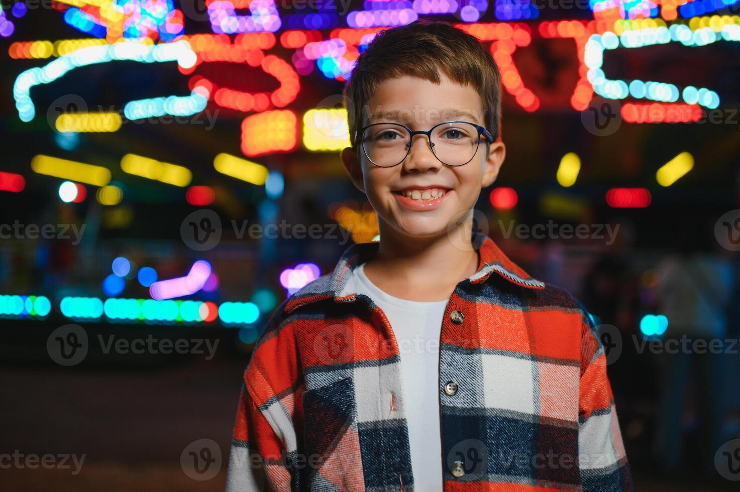 A cute Caucasian boy, a child, came to the amusement park to have fun, play and ride a merry-go-round. A child standing in front of a merry go round photo