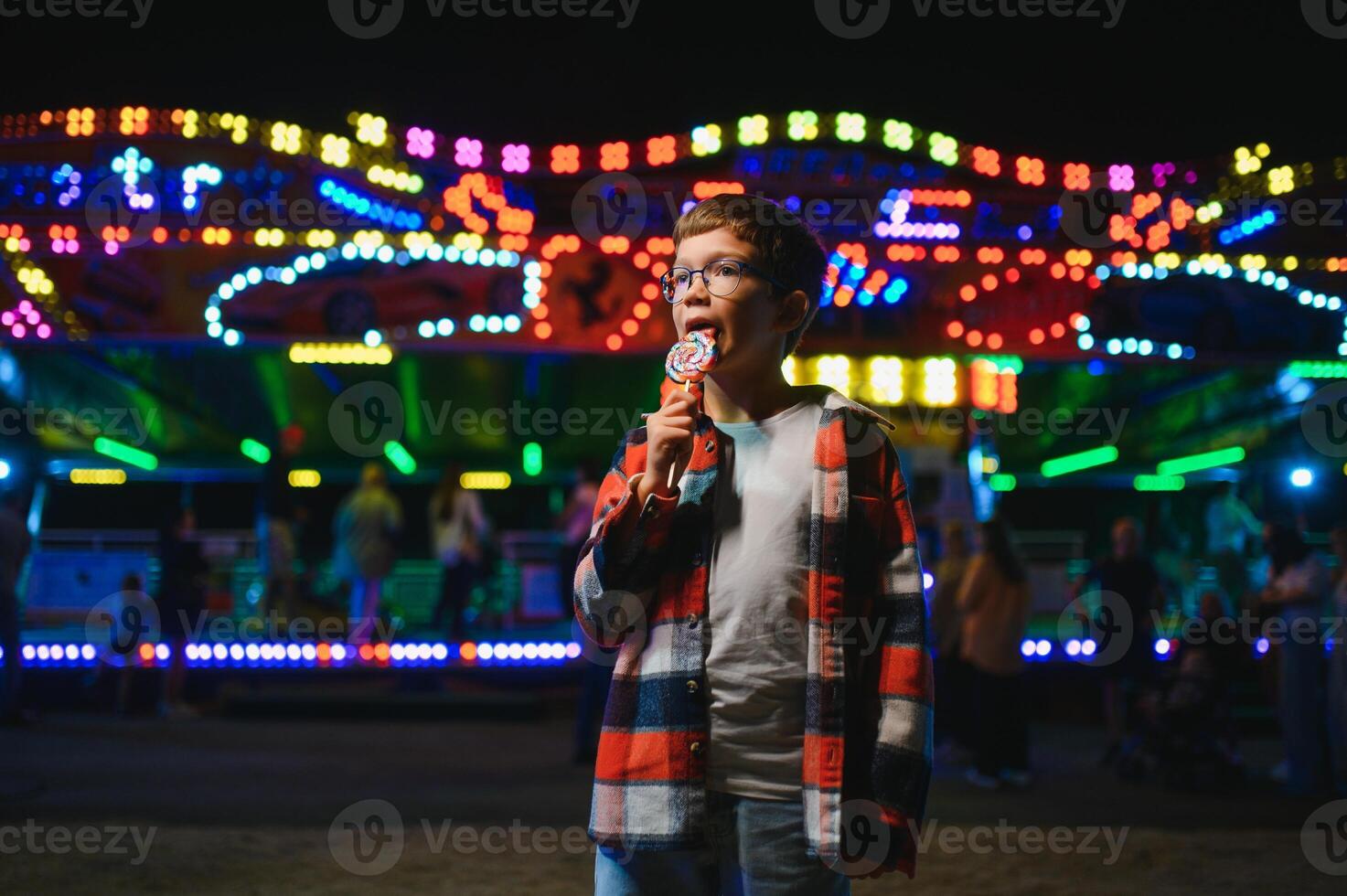 A cute Caucasian boy, a child, came to the amusement park to have fun, play and ride a merry-go-round. A child standing in front of a merry go round photo