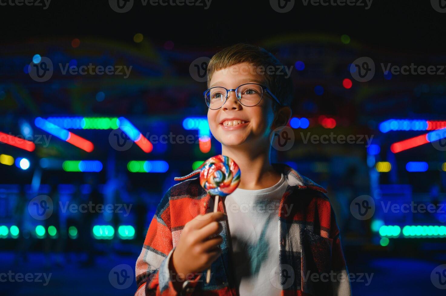 A cute Caucasian boy, a child, came to the amusement park to have fun, play and ride a merry-go-round. A child standing in front of a merry go round photo