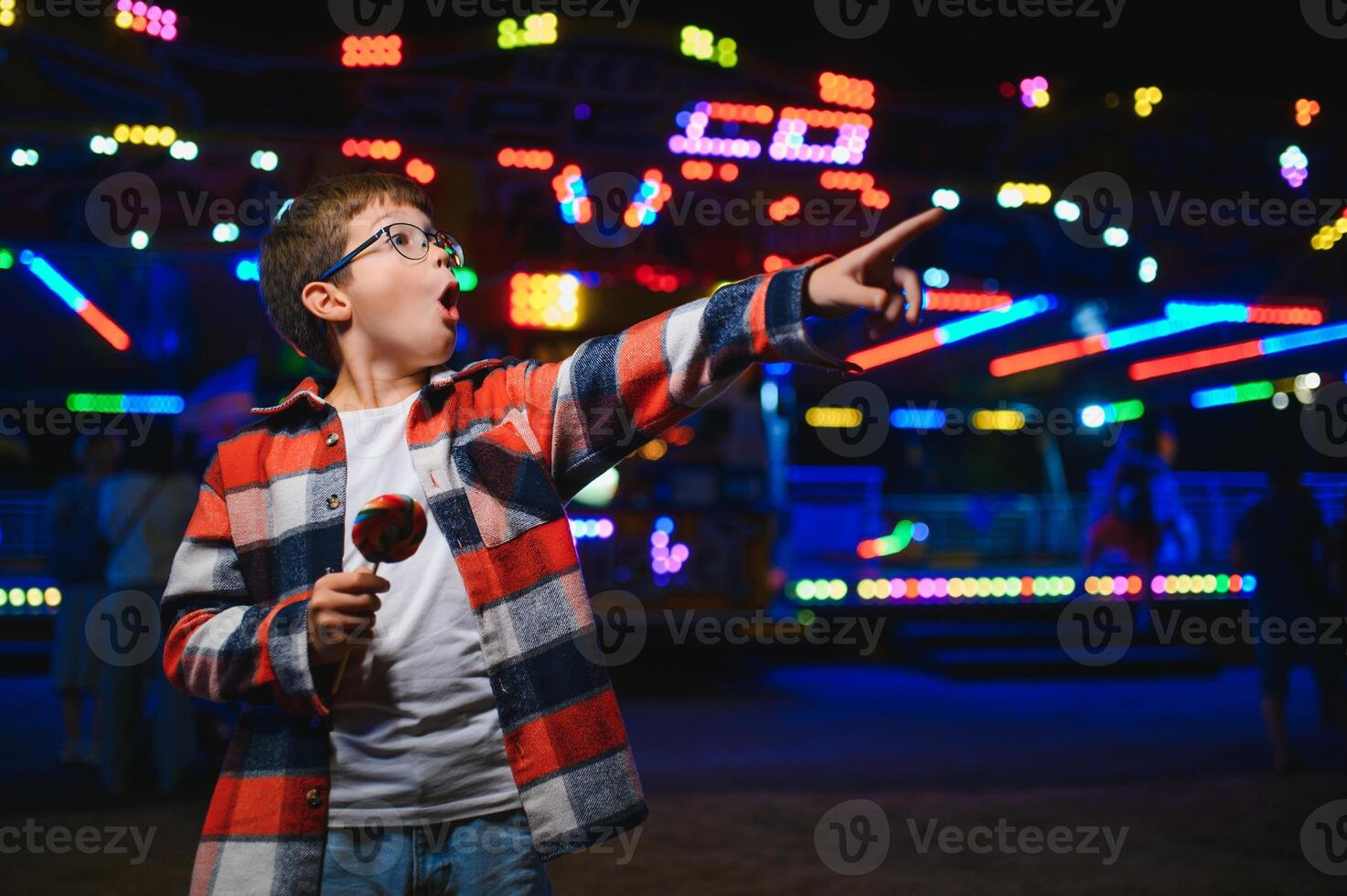 A cute Caucasian boy, a child, came to the amusement park to have fun, play and ride a merry-go-round. A child standing in front of a merry go round photo