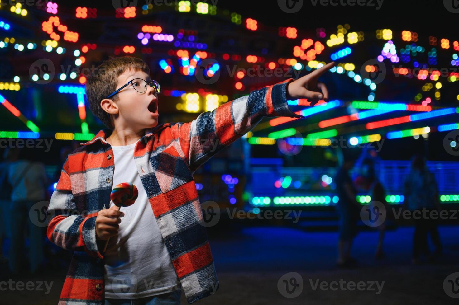 A cute Caucasian boy, a child, came to the amusement park to have fun, play and ride a merry-go-round. A child standing in front of a merry go round photo