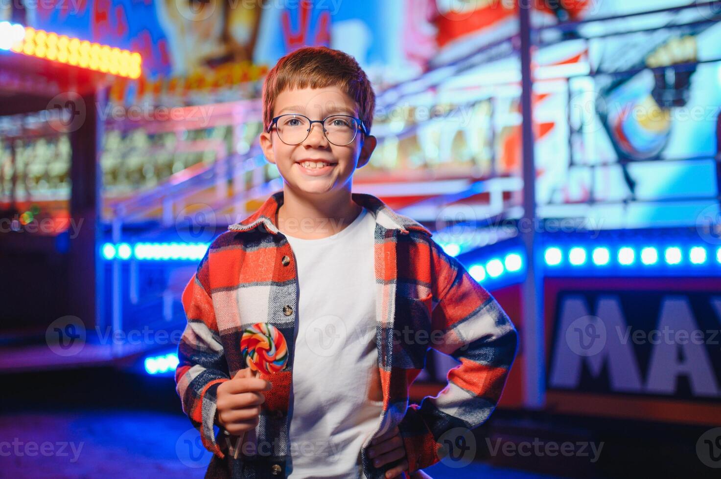 A cute Caucasian boy, a child, came to the amusement park to have fun, play and ride a merry-go-round. A child standing in front of a merry go round photo