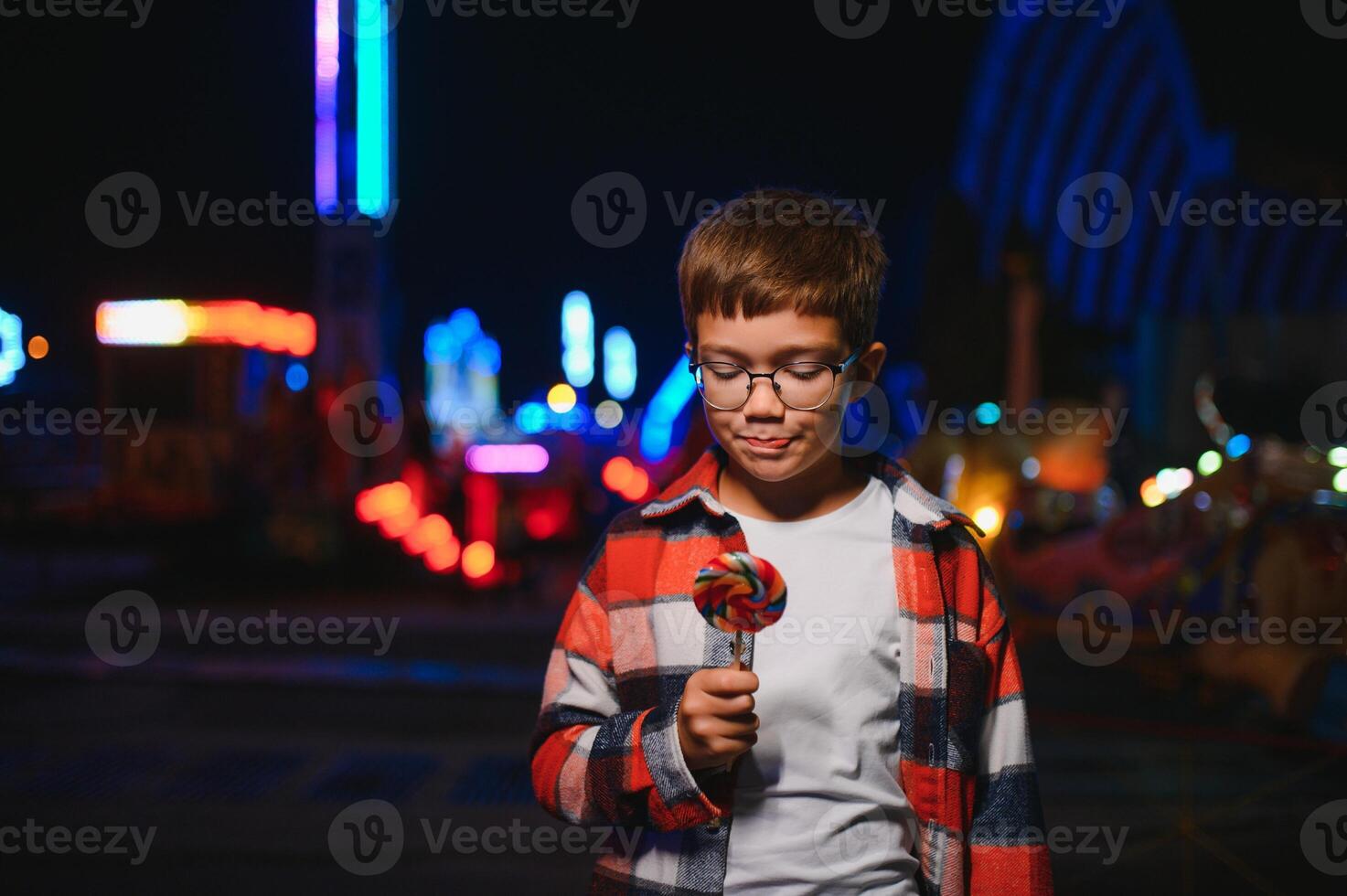 A cute Caucasian boy, a child, came to the amusement park to have fun, play and ride a merry-go-round. A child standing in front of a merry go round photo