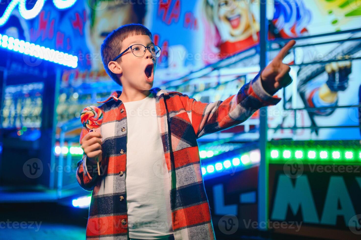 A cute Caucasian boy, a child, came to the amusement park to have fun, play and ride a merry-go-round. A child standing in front of a merry go round photo