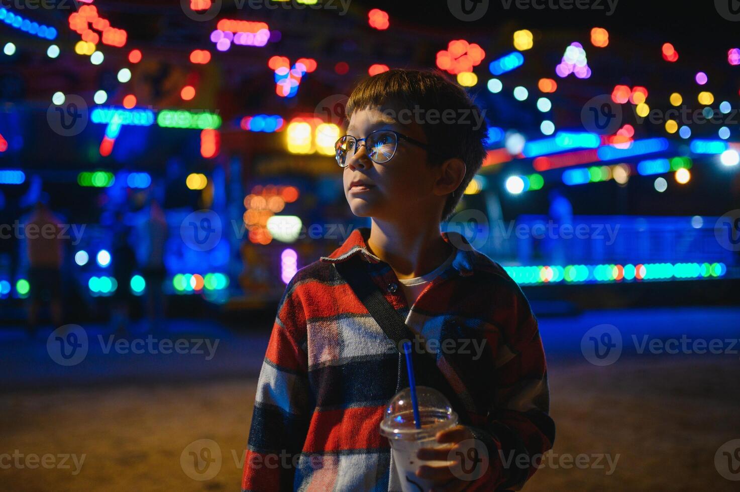 A cute Caucasian boy, a child, came to the amusement park to have fun, play and ride a merry-go-round. A child standing in front of a merry go round photo