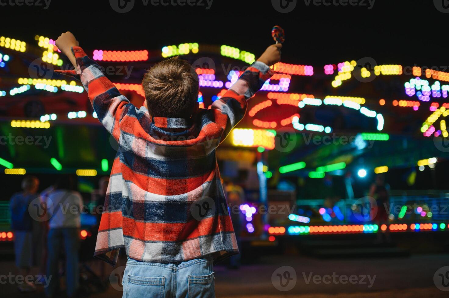 A cute Caucasian boy, a child, came to the amusement park to have fun, play and ride a merry-go-round. A child standing in front of a merry go round photo