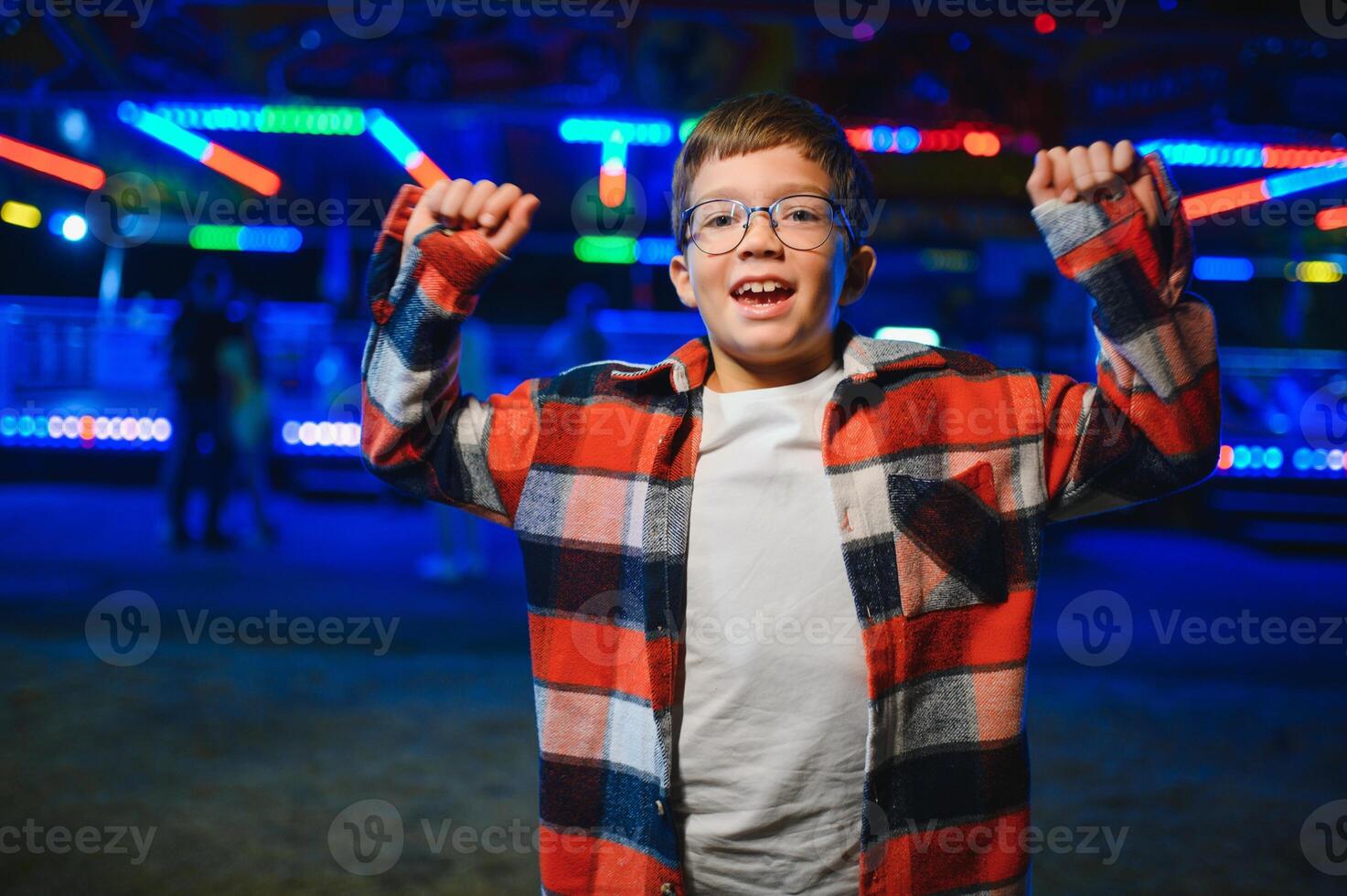 A cute Caucasian boy, a child, came to the amusement park to have fun, play and ride a merry-go-round. A child standing in front of a merry go round photo