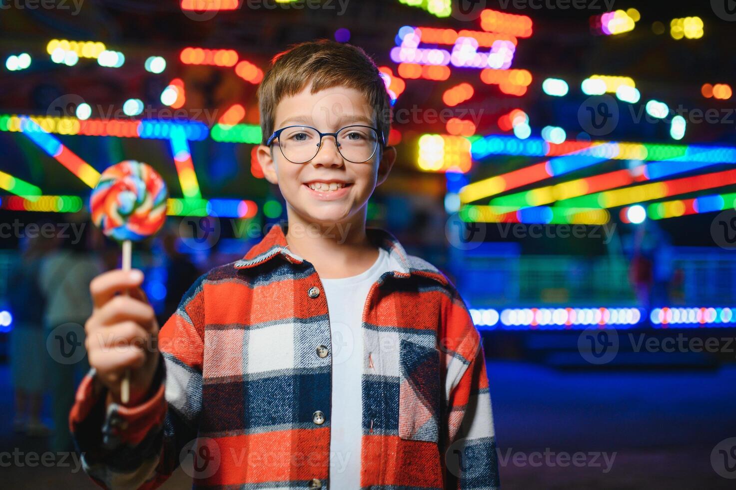 A cute Caucasian boy, a child, came to the amusement park to have fun, play and ride a merry-go-round. A child standing in front of a merry go round photo