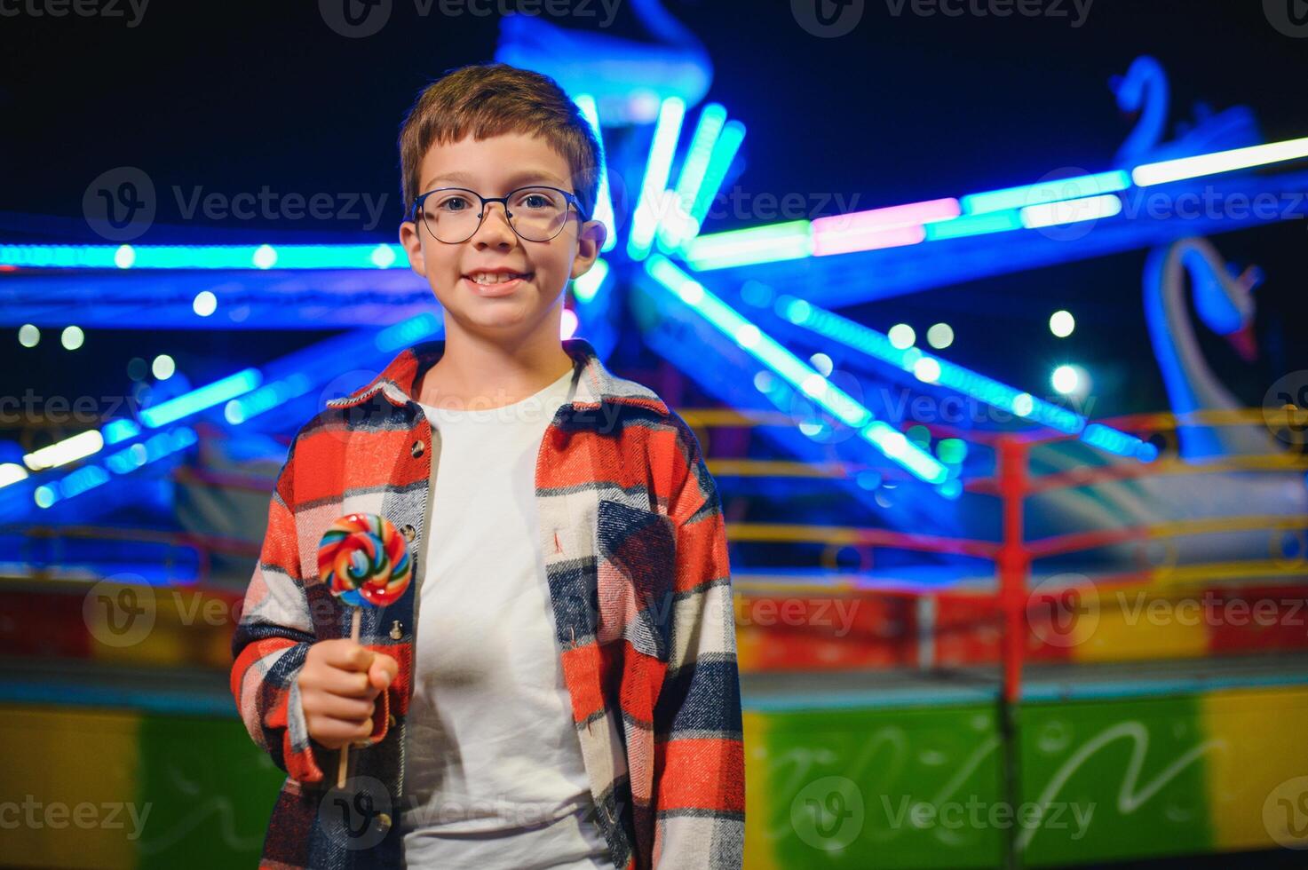 A cute Caucasian boy, a child, came to the amusement park to have fun, play and ride a merry-go-round. A child standing in front of a merry go round photo