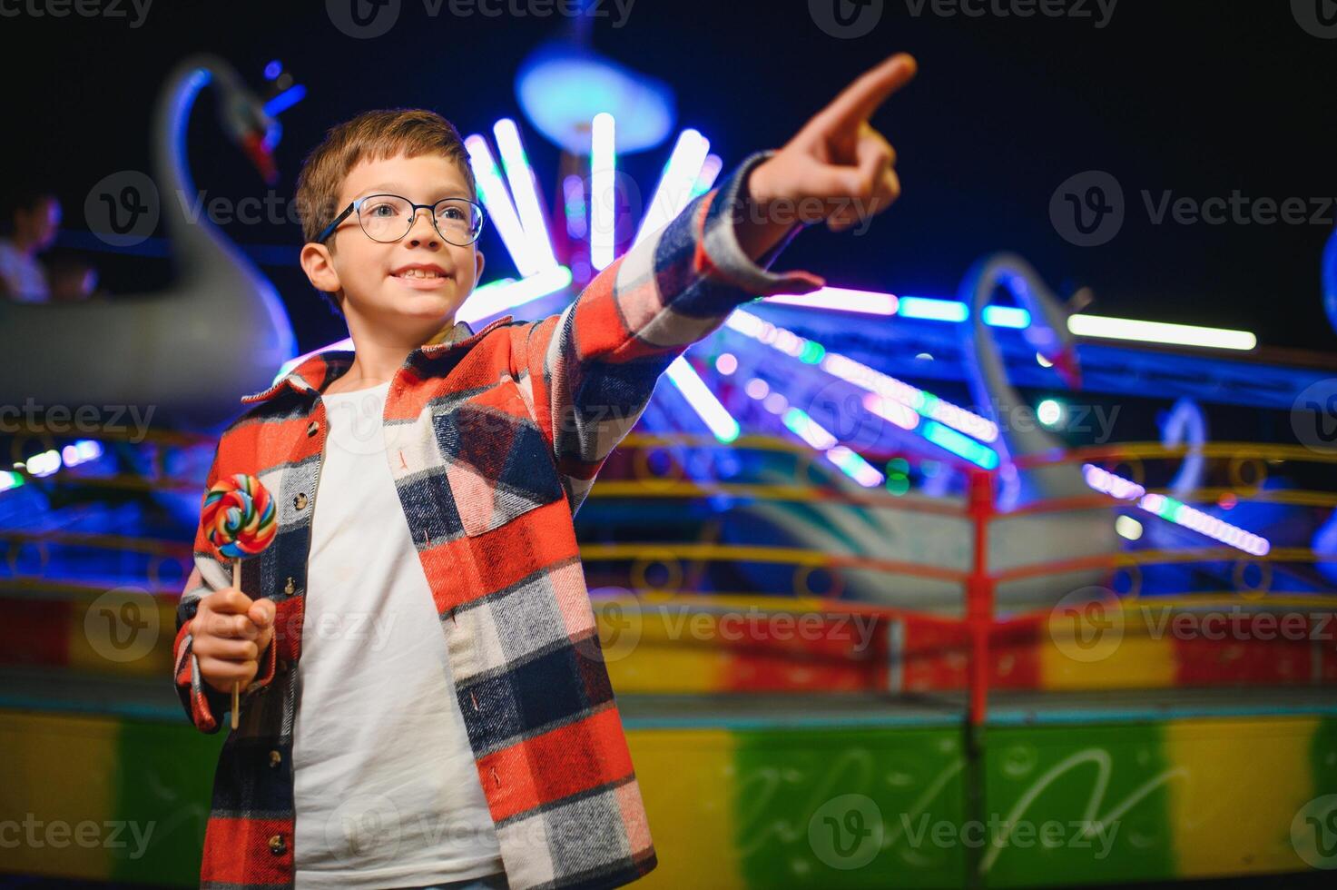 A cute Caucasian boy, a child, came to the amusement park to have fun, play and ride a merry-go-round. A child standing in front of a merry go round photo