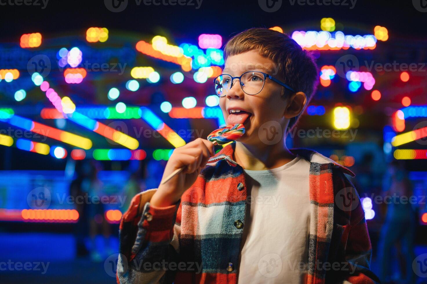 A cute Caucasian boy, a child, came to the amusement park to have fun, play and ride a merry-go-round. A child standing in front of a merry go round photo