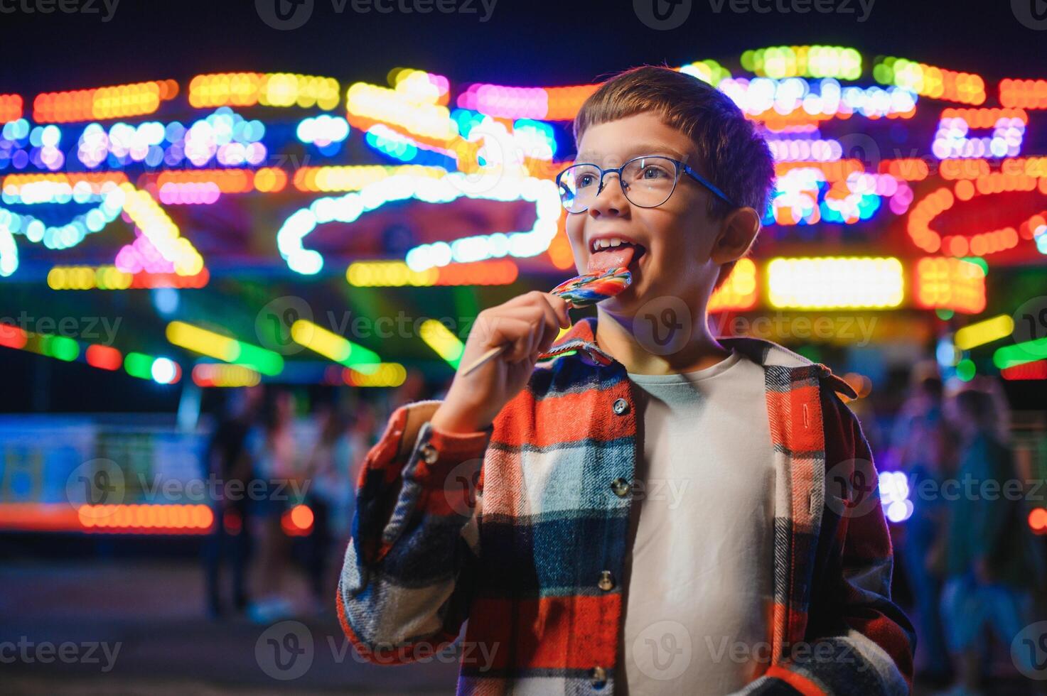 A cute Caucasian boy, a child, came to the amusement park to have fun, play and ride a merry-go-round. A child standing in front of a merry go round photo