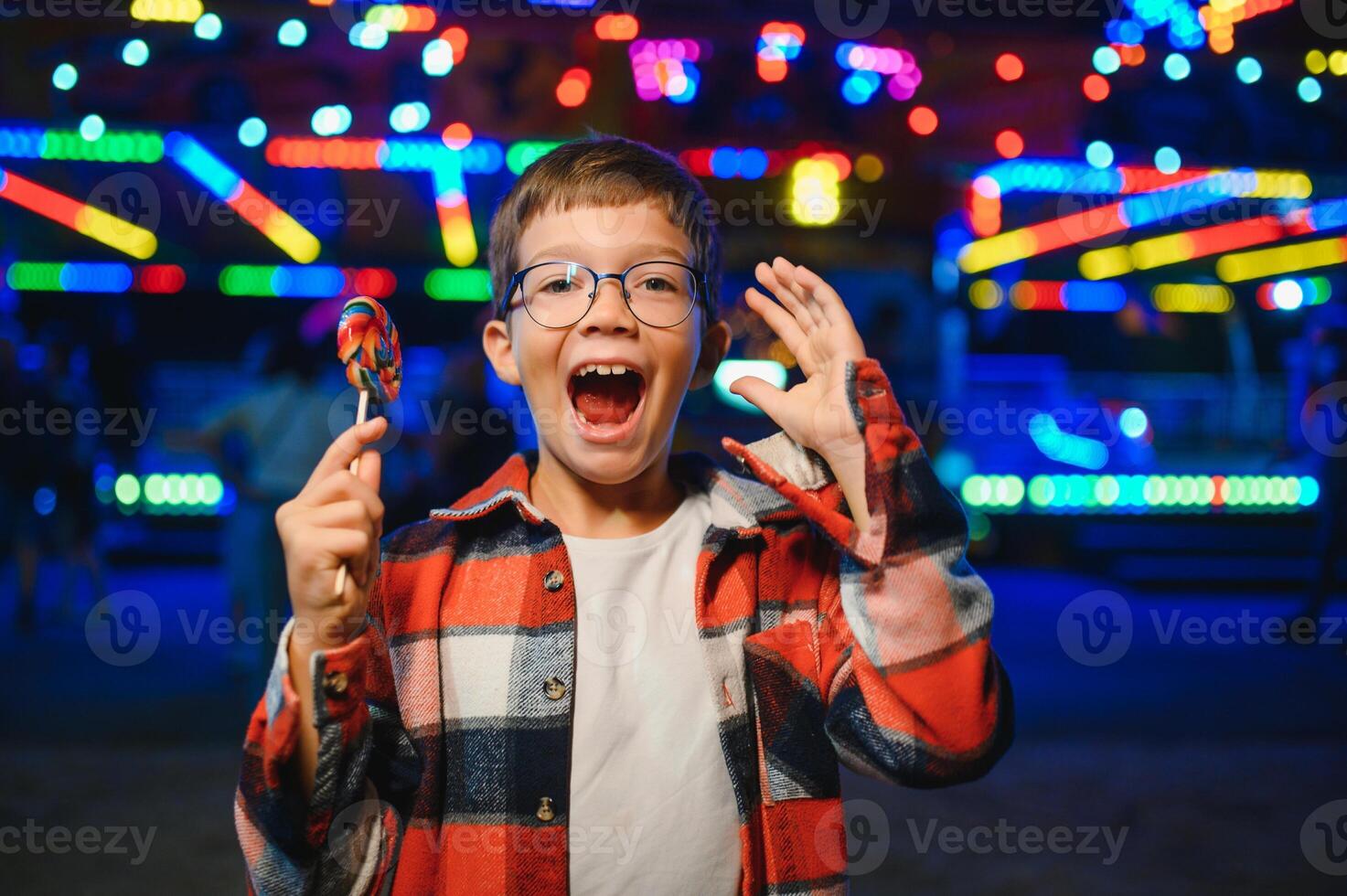A cute Caucasian boy, a child, came to the amusement park to have fun, play and ride a merry-go-round. A child standing in front of a merry go round photo