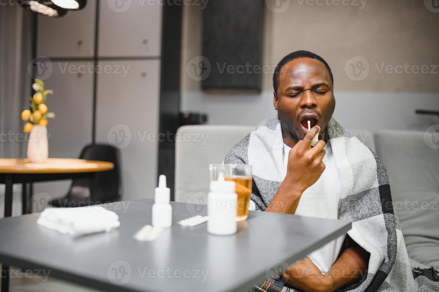 Man experiencing sore throat pain using throat spray for relief on couch at home photo