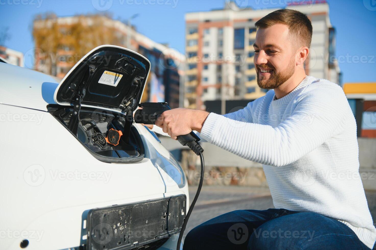young handsome man holding charging cable at electric charging station point standing near his new car. photo