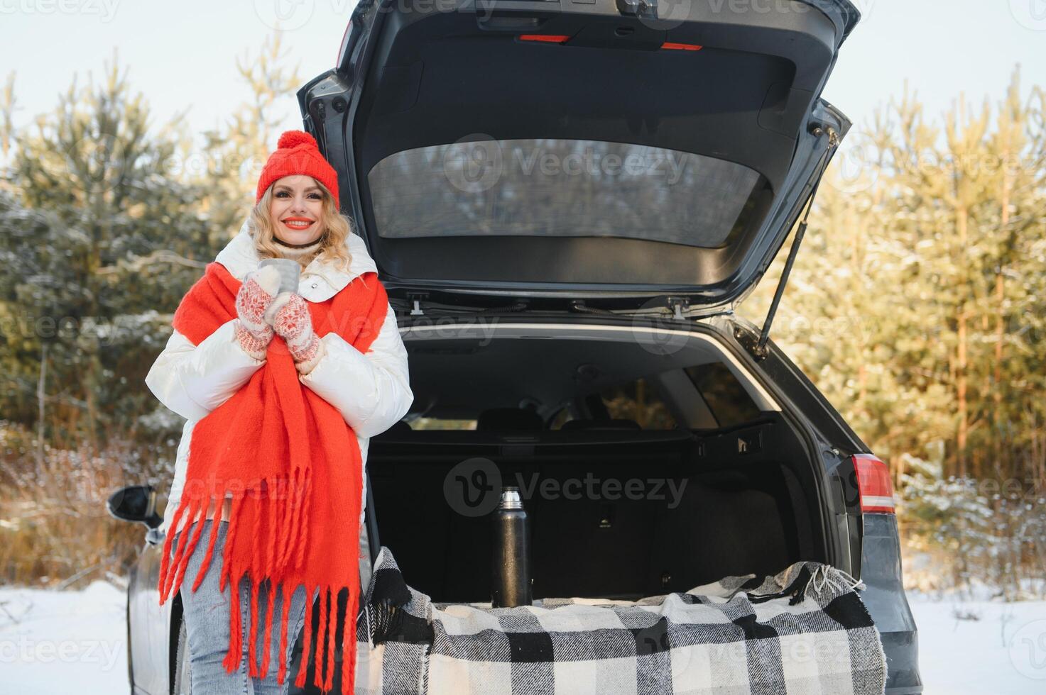 With cup of drink. Beautiful young woman is outdoors near her automobile at winter time. photo