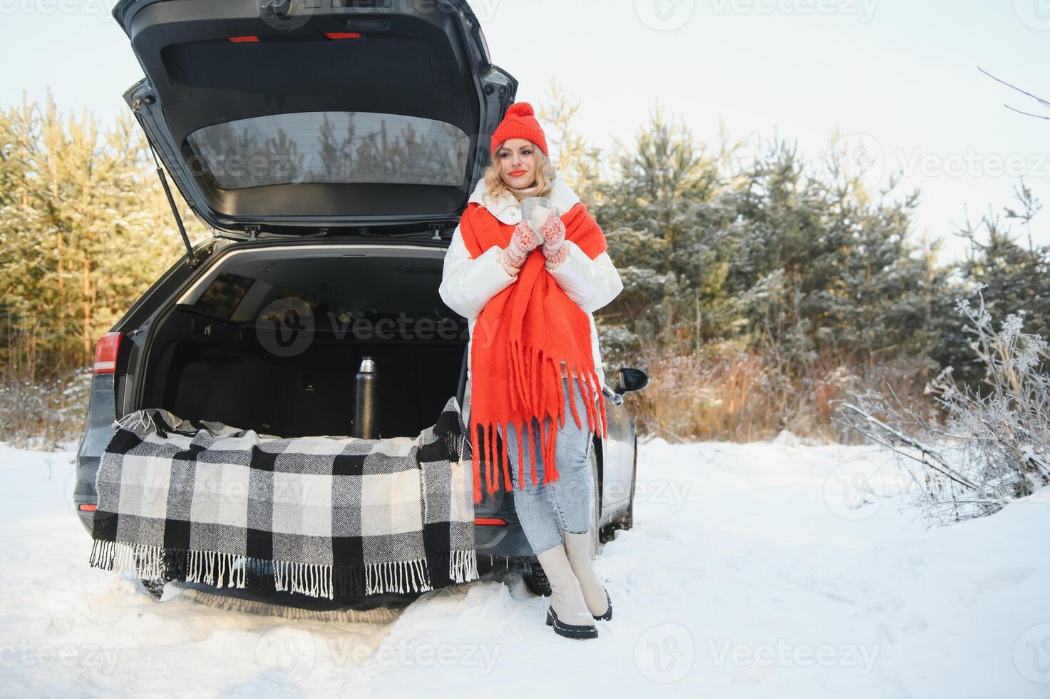 young woman sitting in car trunk drinking warm tea and takes a selfie at winter snowed day. photo