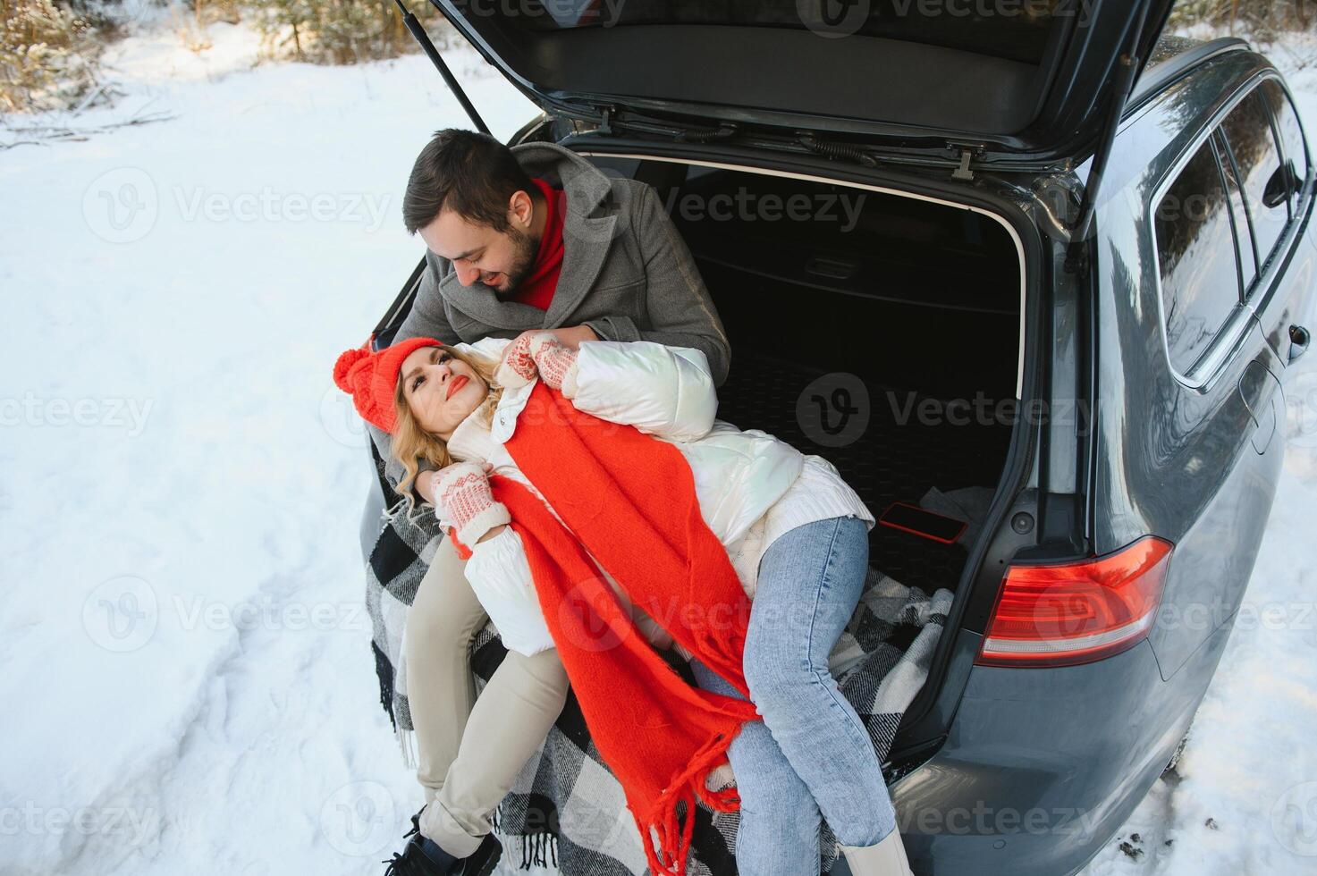 Happy couple sitting in open car back, having stop off. Romantic traveling concept. Winter forest. photo
