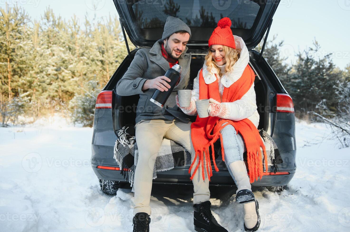 Happy couple sitting in open car back, having stop off. Romantic traveling concept. Winter forest. photo