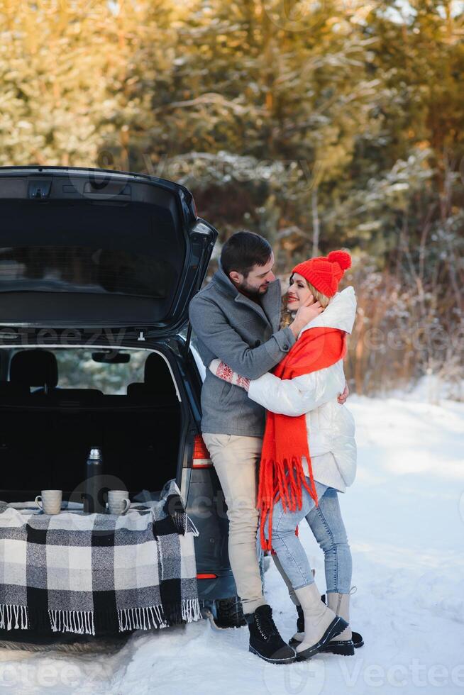Smiling together. Nice couple have weekend at countryside at winter time. Sitting on the rear part of modern car. photo