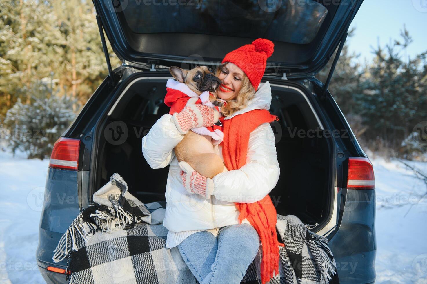 Woman resting in the winter forest sitting in the open trunk of a car with a dog. photo