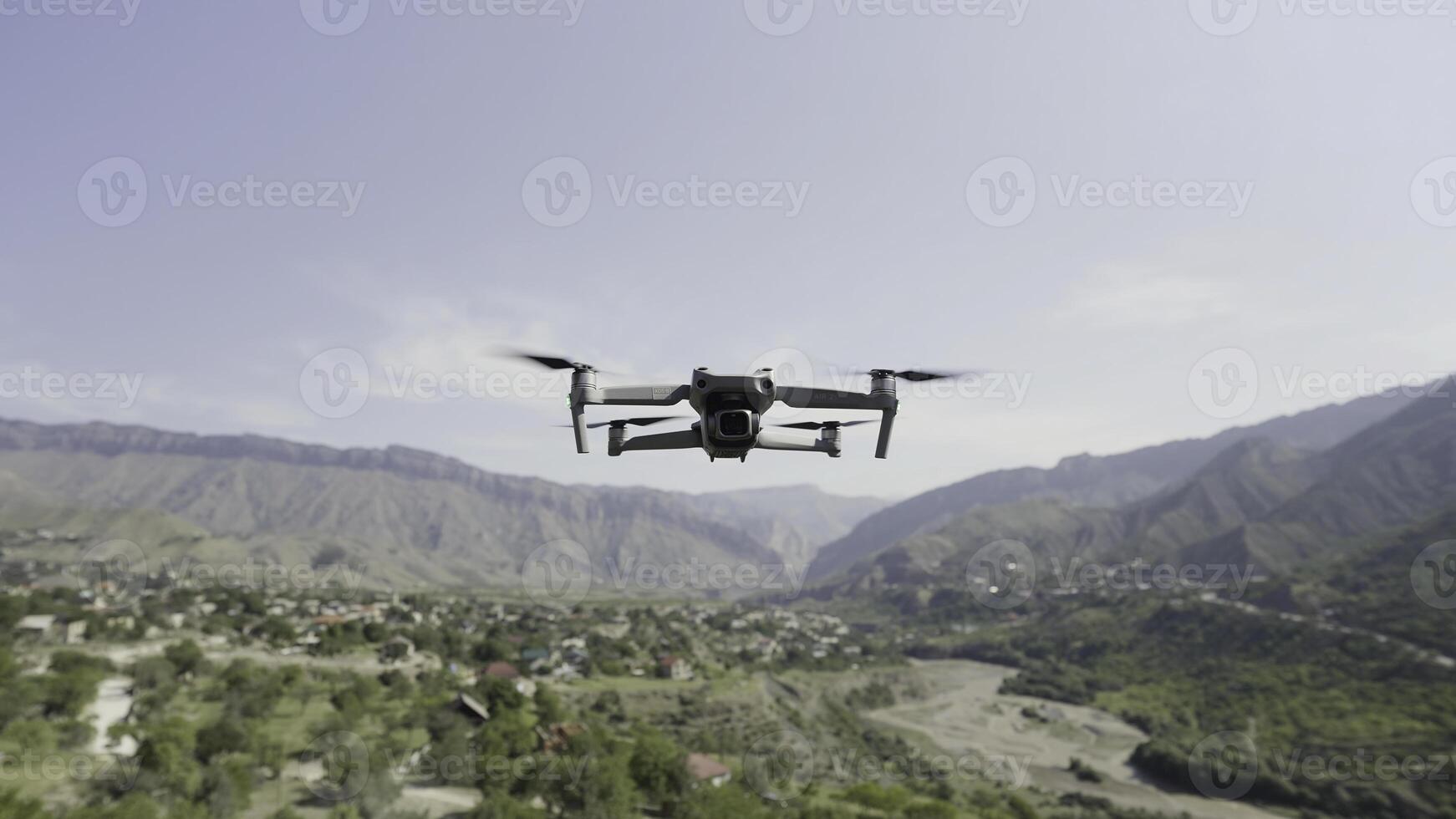 Quadcopter hanging in the air above green valley and growing trees. Action. Drone with spinning blades above mountains on cloudy sky backgrounds. photo