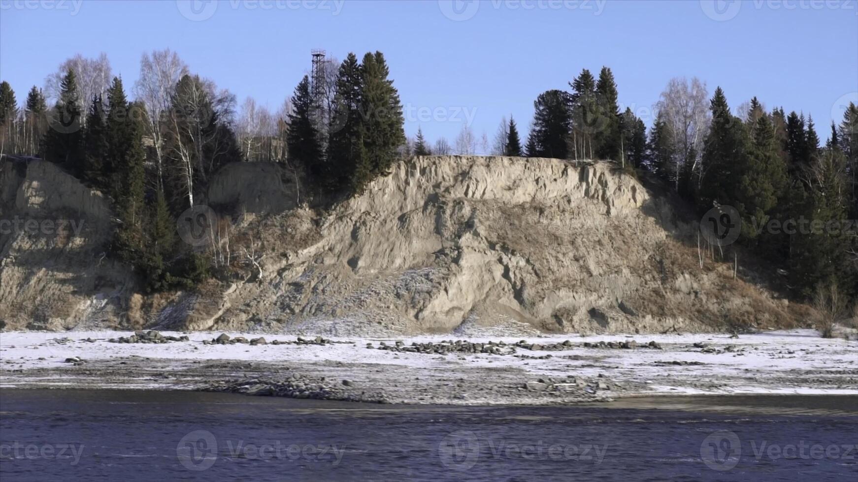 Natural landscape with a river in early winter and a hilly shore covered by trees. Clip. Stone cliff with forest and cold river. photo