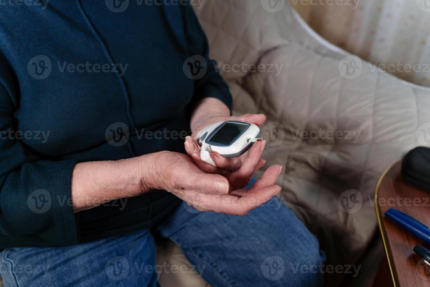 Mature woman's weathered hands using a portable glucose meter to monitor her blood sugar levels at home. self care and personal health management photo