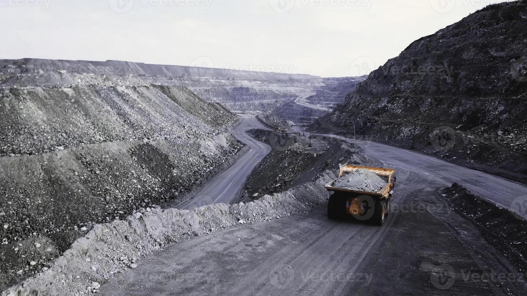 Dump truck is at quarry. Top view of driving orange dump truck with rubble on road open pit. Heavy transport in mining industry photo