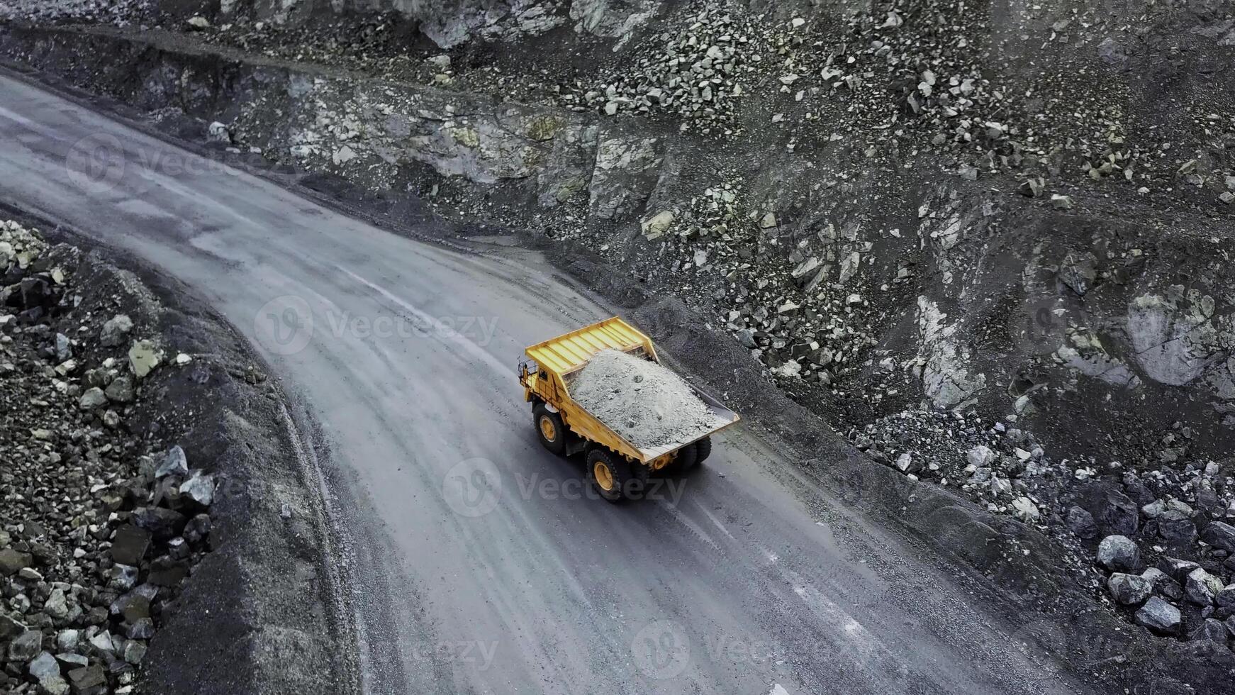 Dump truck is at quarry. Top view of driving orange dump truck with rubble on road open pit. Heavy transport in mining industry photo