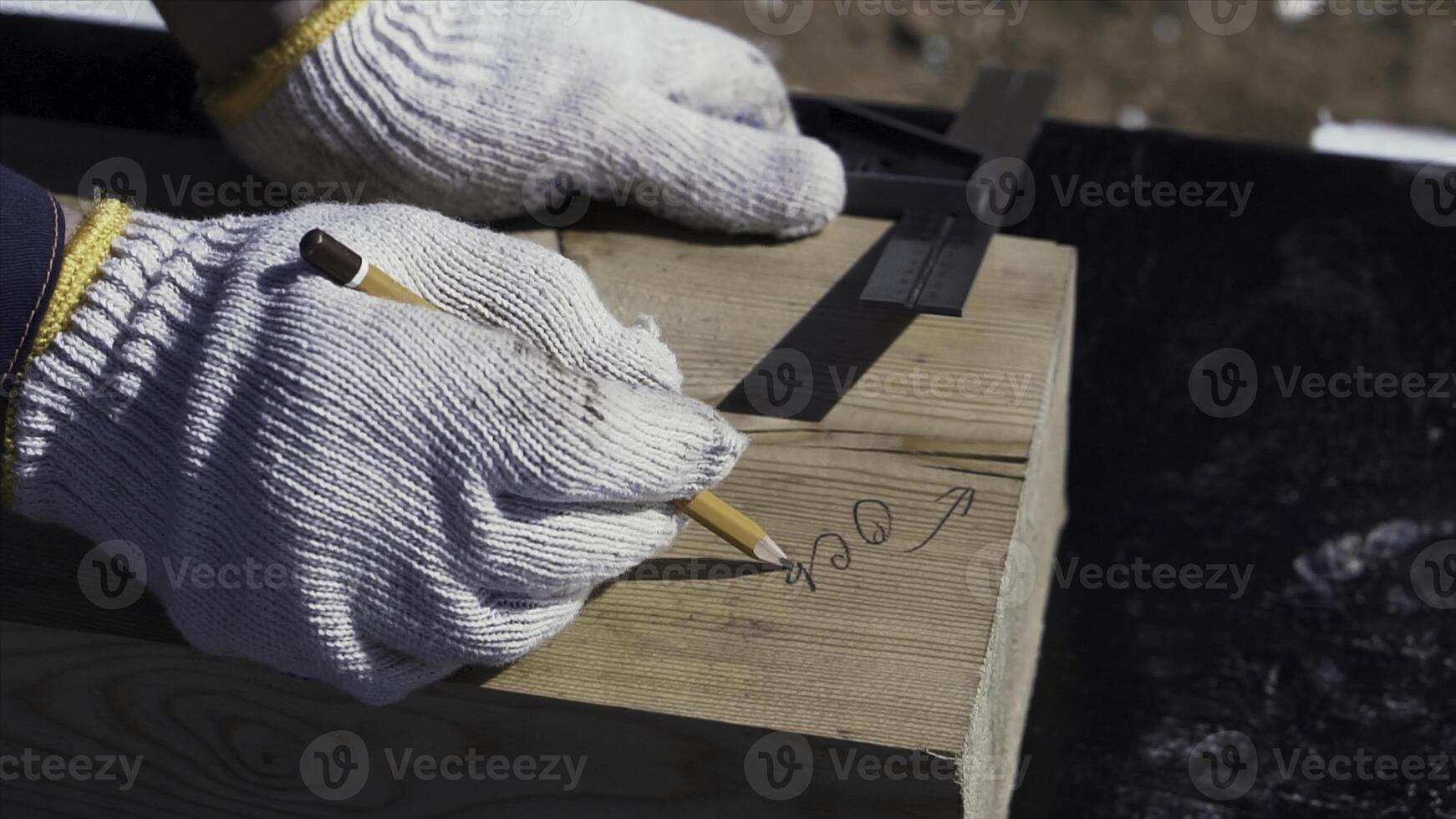 Close up for hands of a carpenter in protective gloves writing something on a wooden board. Clip. Joinery works, measuring and marking the wood, woodwork and furniture making concept. photo