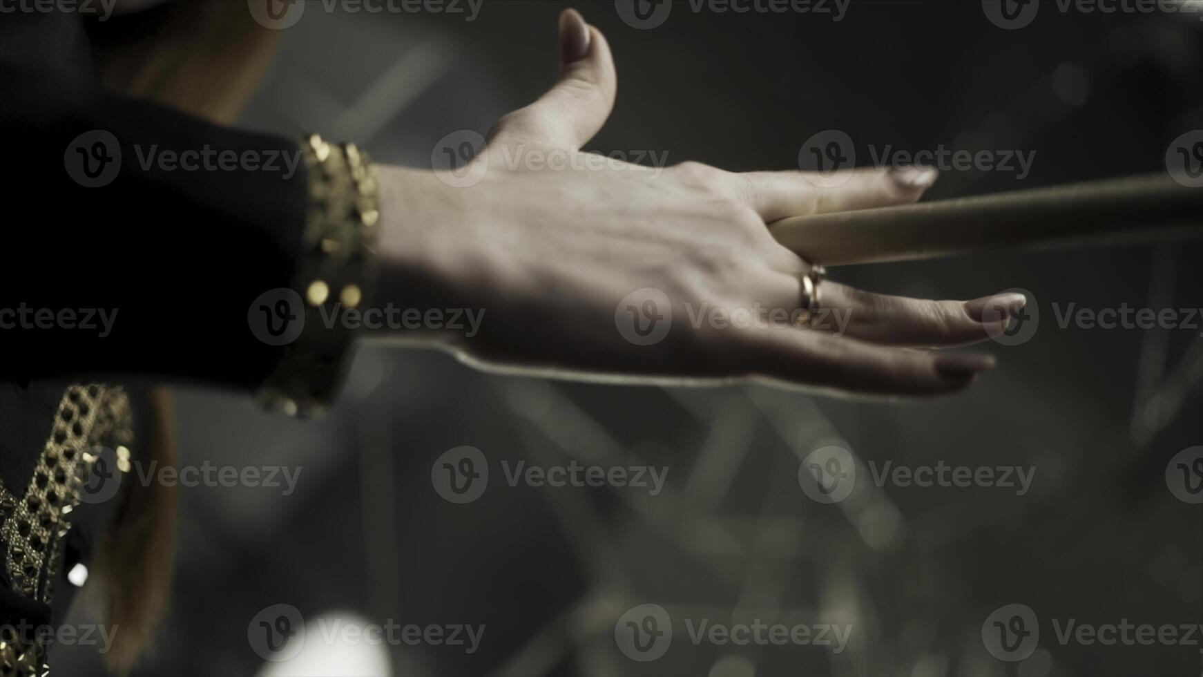 Young attractive woman hand holding drumstick and rotating it during musical rehearsal. Action. Close up for woman hand with manicure and gold rings holding and spinning a drumstick. photo