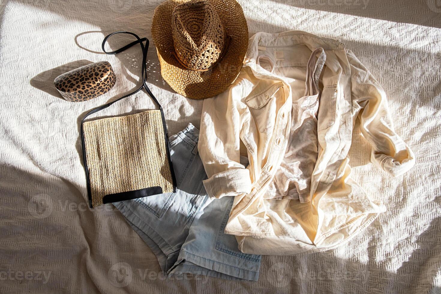 Casual summer outfit arrangement on bed, featuring light clothing and stylish hat. photo