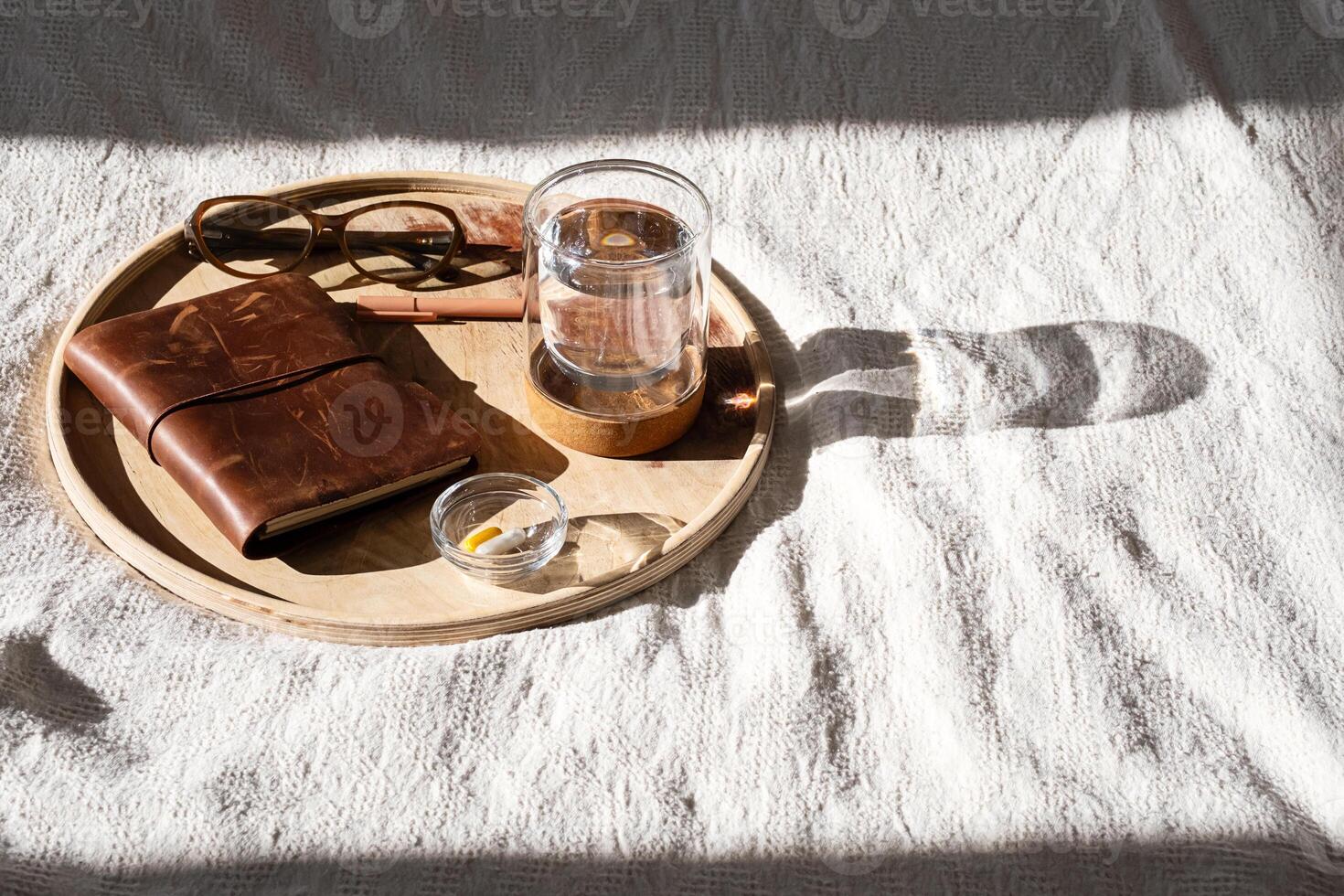 Wooden tray displaying vitamin dose, glass of water, notebook and glasses. Morning routine concepts. photo