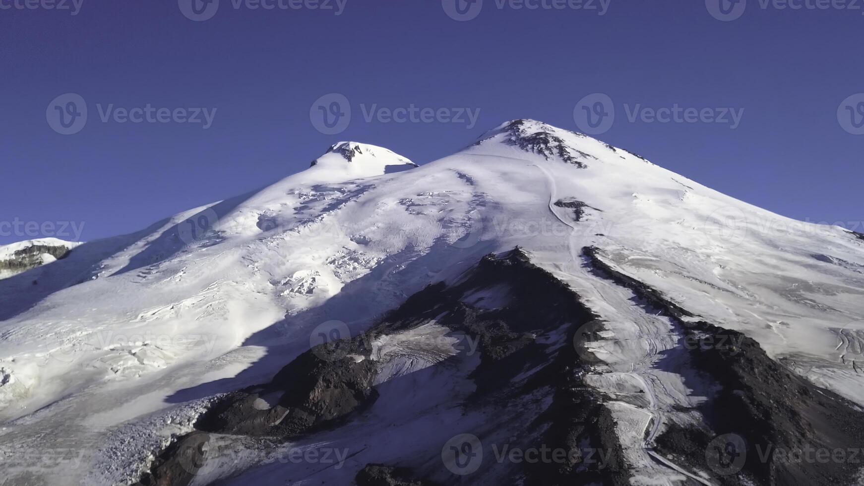 Snowy and icy mountain peaks of glaciers in Austrian Alps at winter. Clip. Aerial view of a snowy slope of a huge rock on blue sky background. photo