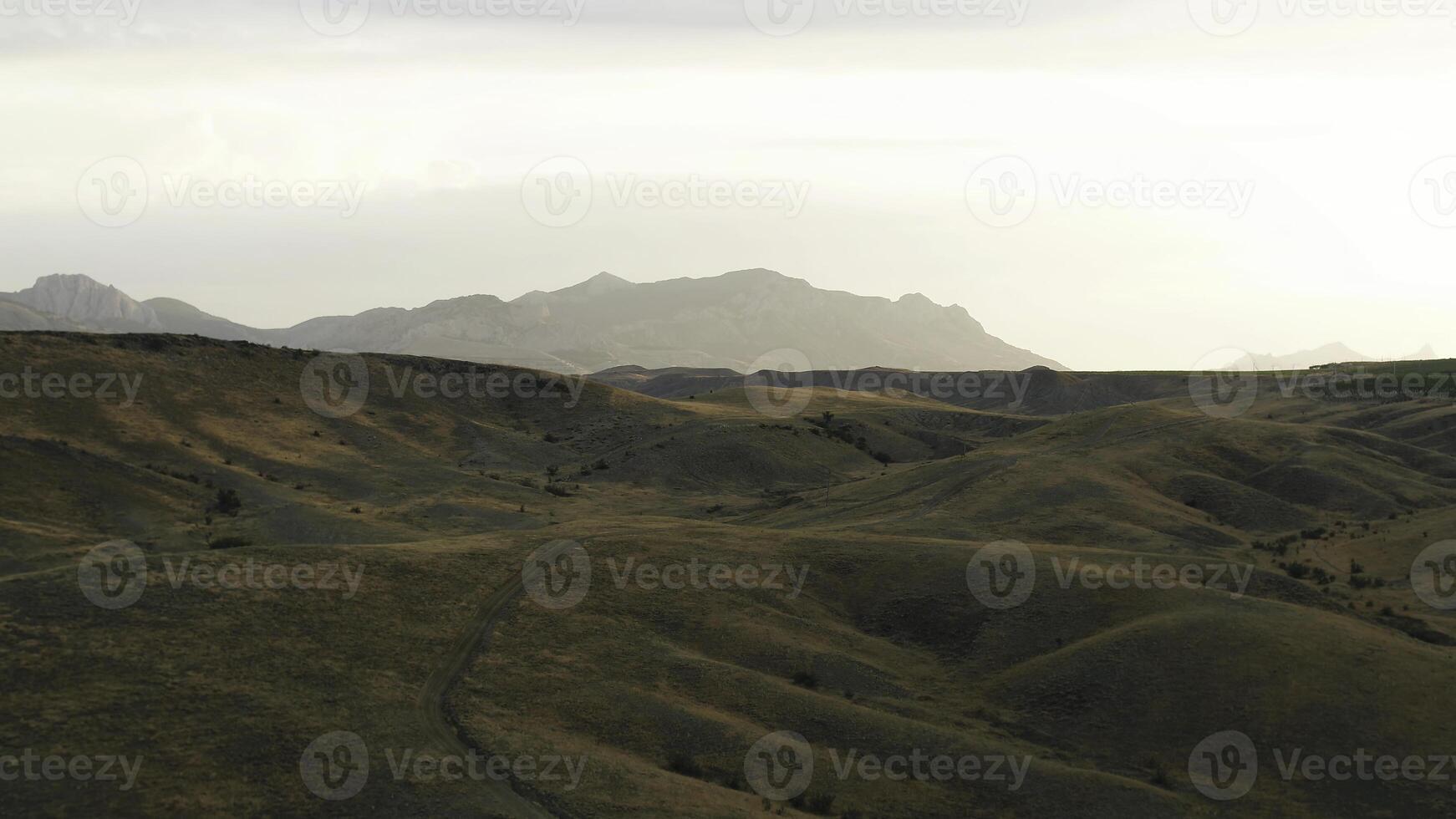 Aerial view of country roads in hilly region with mountains on the background shrouded in fog. Shot. Flying over the mountains covered by golden grass. photo