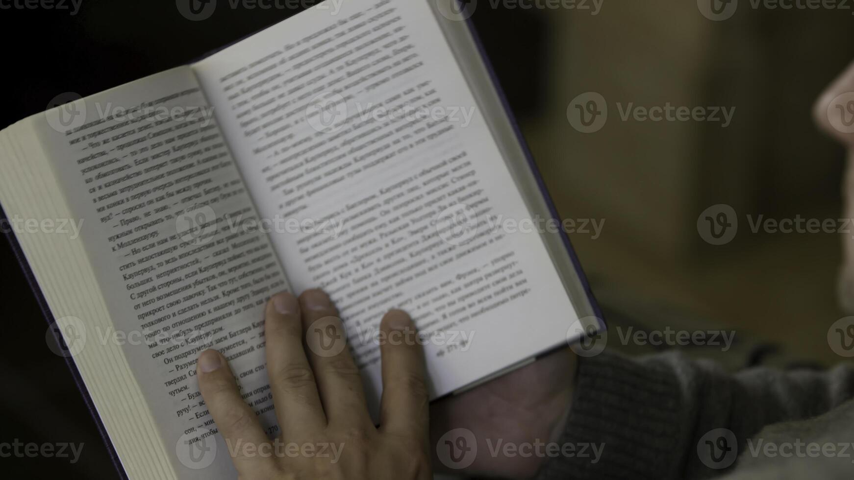 Over the shoulder view of a man reading a book at home. . Middle aged male sitting and reading a paper book, turning pages, relaxing at home. photo
