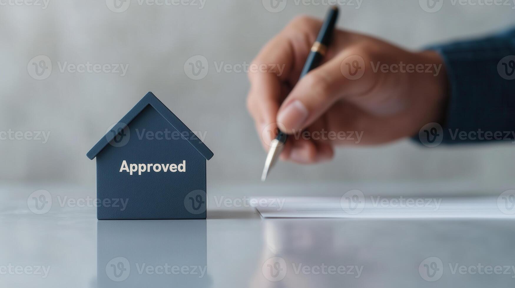 A hand signing a document with a small house model labeled 'Approved' nearby, showcasing the concept of property approval and real estate transactions against a soft background. photo
