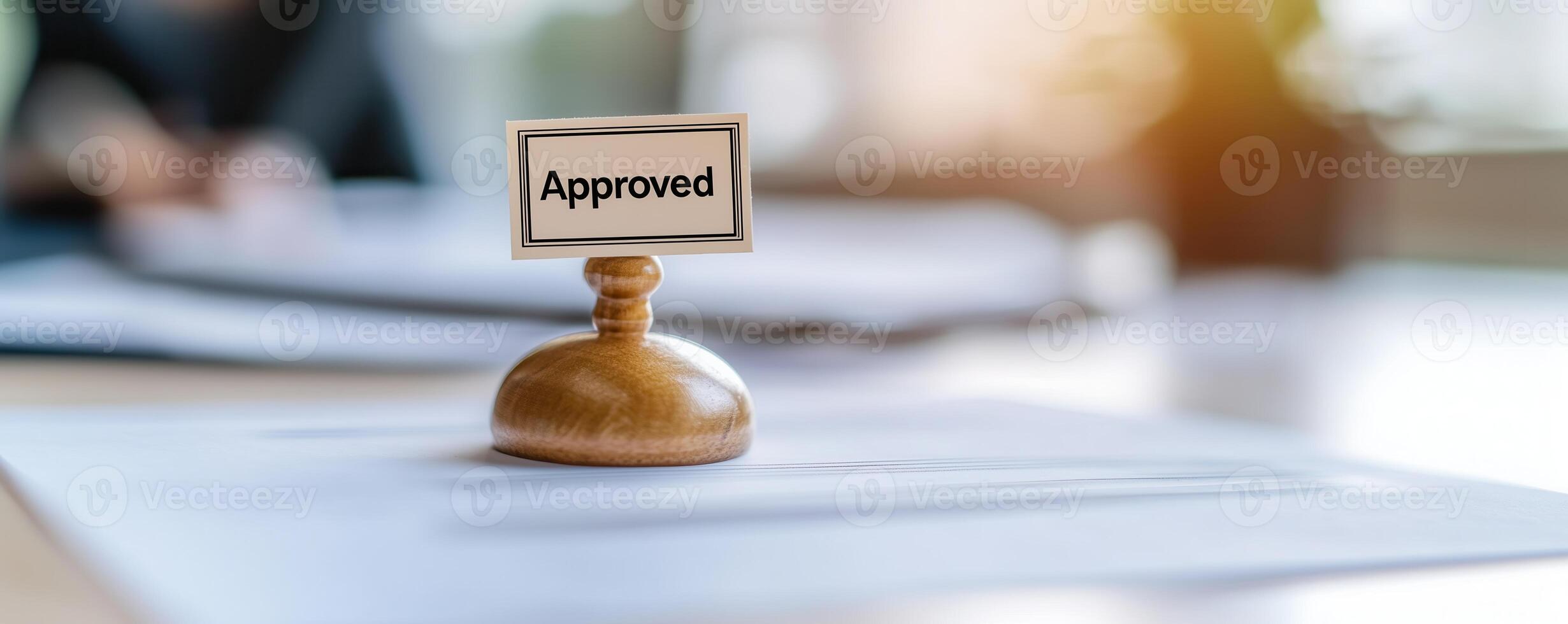 A wooden stamp with the word 'Approved' placed on documents, symbolizing success, acceptance, and validation in a professional setting with a soft focus background. photo