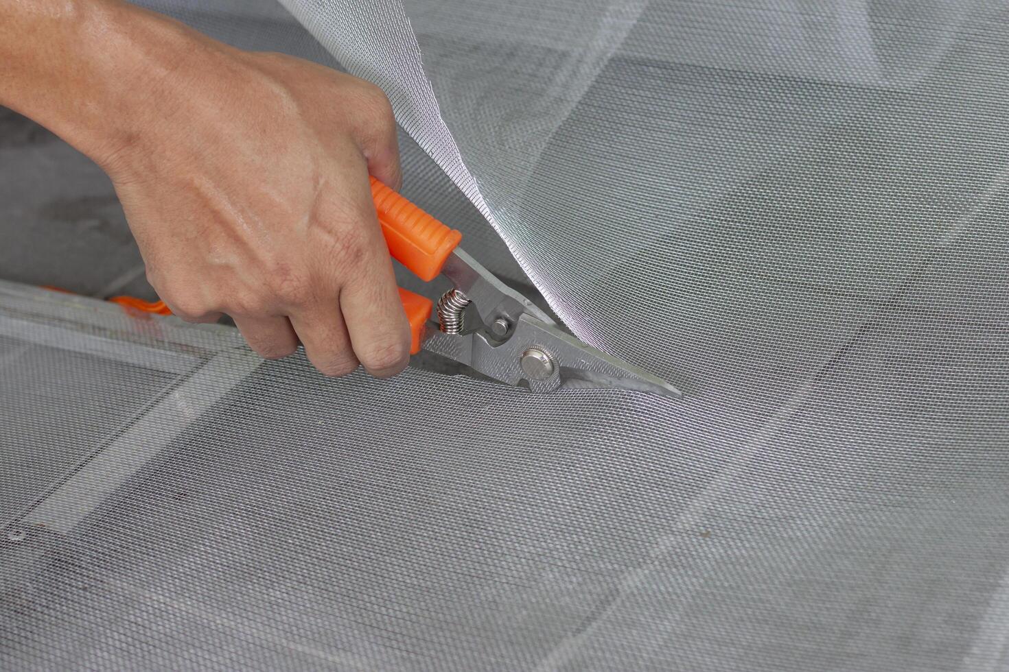 Hand of worker holding scissors to cut mosquito net wire mesh screen this is to be attached to the window of the house to prevent insects. photo