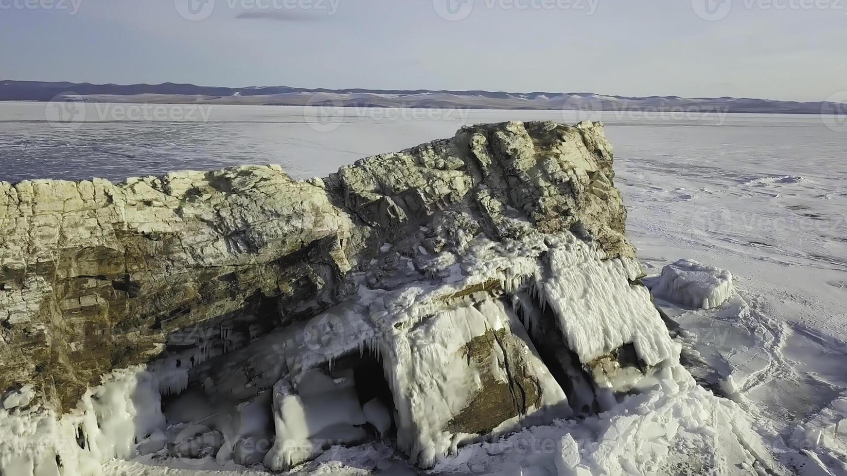 Aerial view of a huge frozen lake covered by snow with a cliff rising up through ice. Clip. Winter landscape of the natural water reservoir and a stony hill. photo