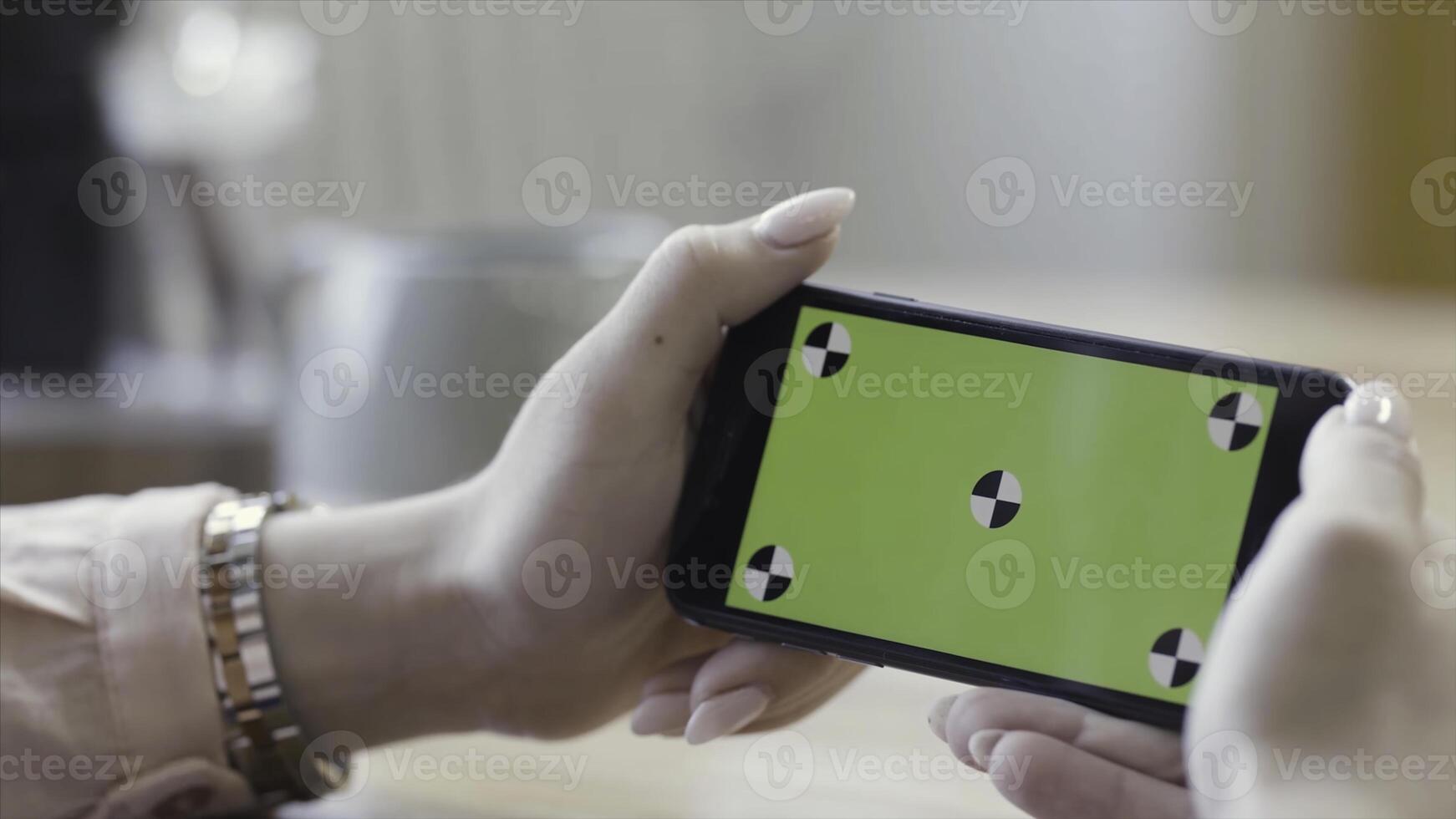 Woman looking at horizontal smartphone with green screen. Stock footage. Close up of beautiful female hands holding mobile phone with chromakey on blurred room background. photo