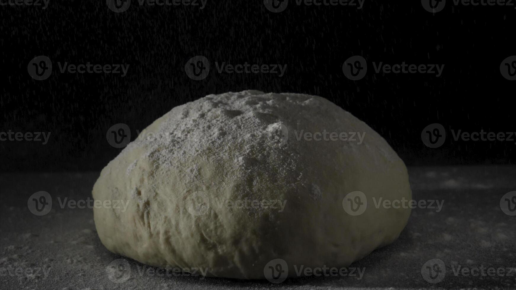Four falling on fresh raw dough on black background in slow motion. Frame. Cook sifts the flour for the dough. Sprinkling flour over fresh dough on kitchen table. Fresh raw dough for pizza or bread photo