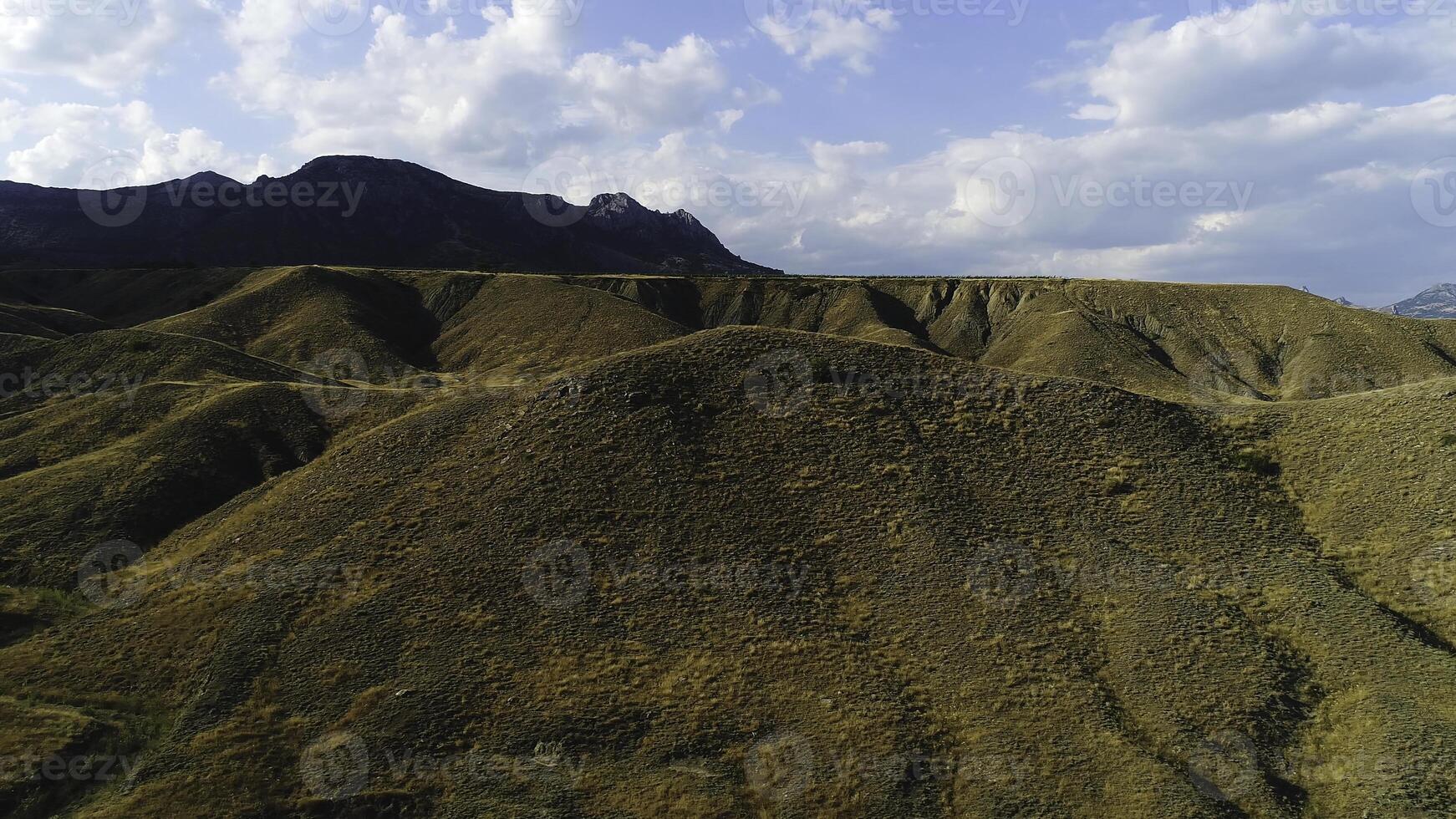 Autumn blue sky with white clouds and mountains withlowed grass. Shot. Aerial of sunset on a background of hills covered with yellow dry grass. photo