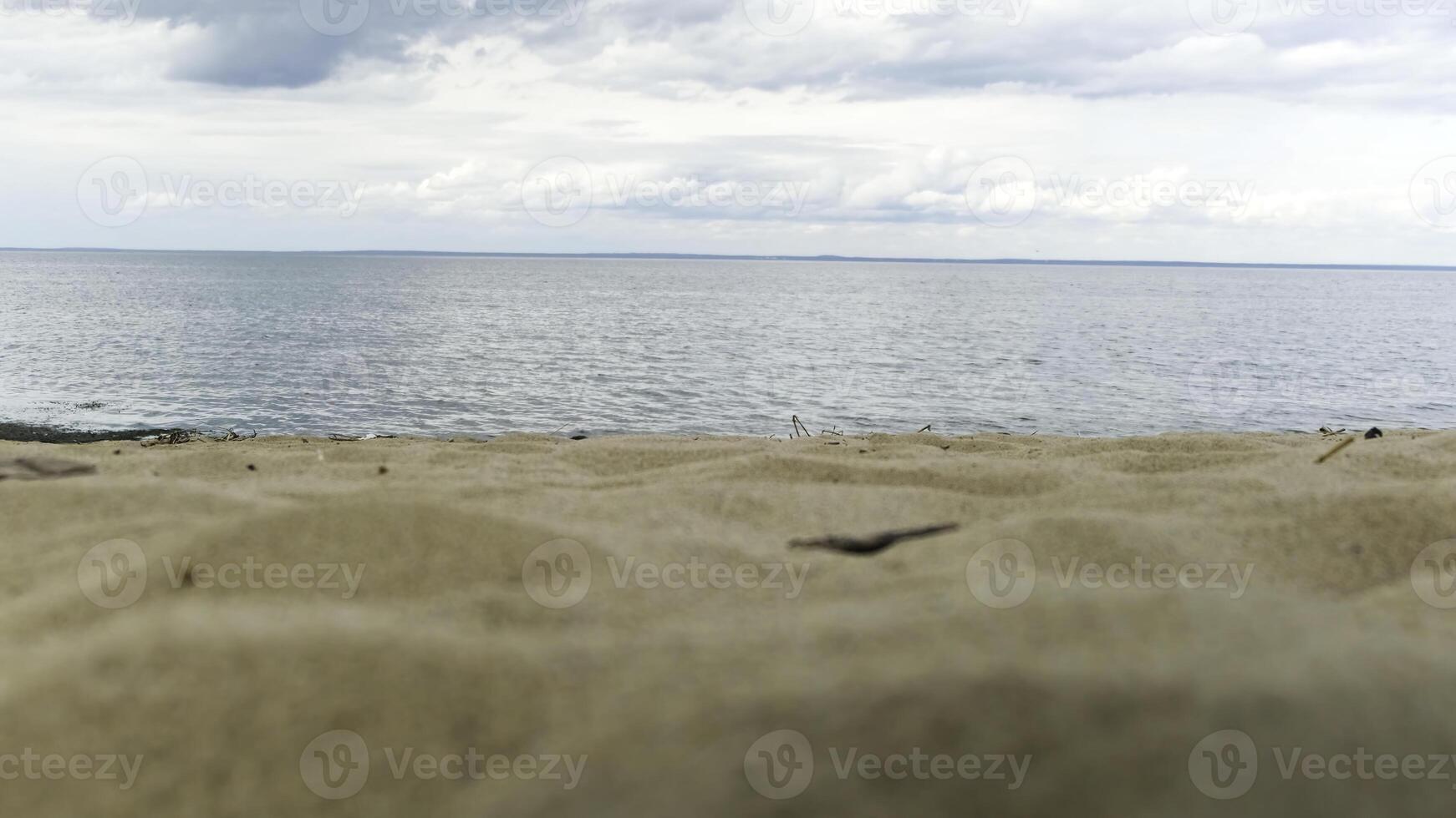 River bank with sand dunes and rippled waterof river on the background. Concept. Close up of sandy shore of a wide river against mountains and cloudy sky. photo