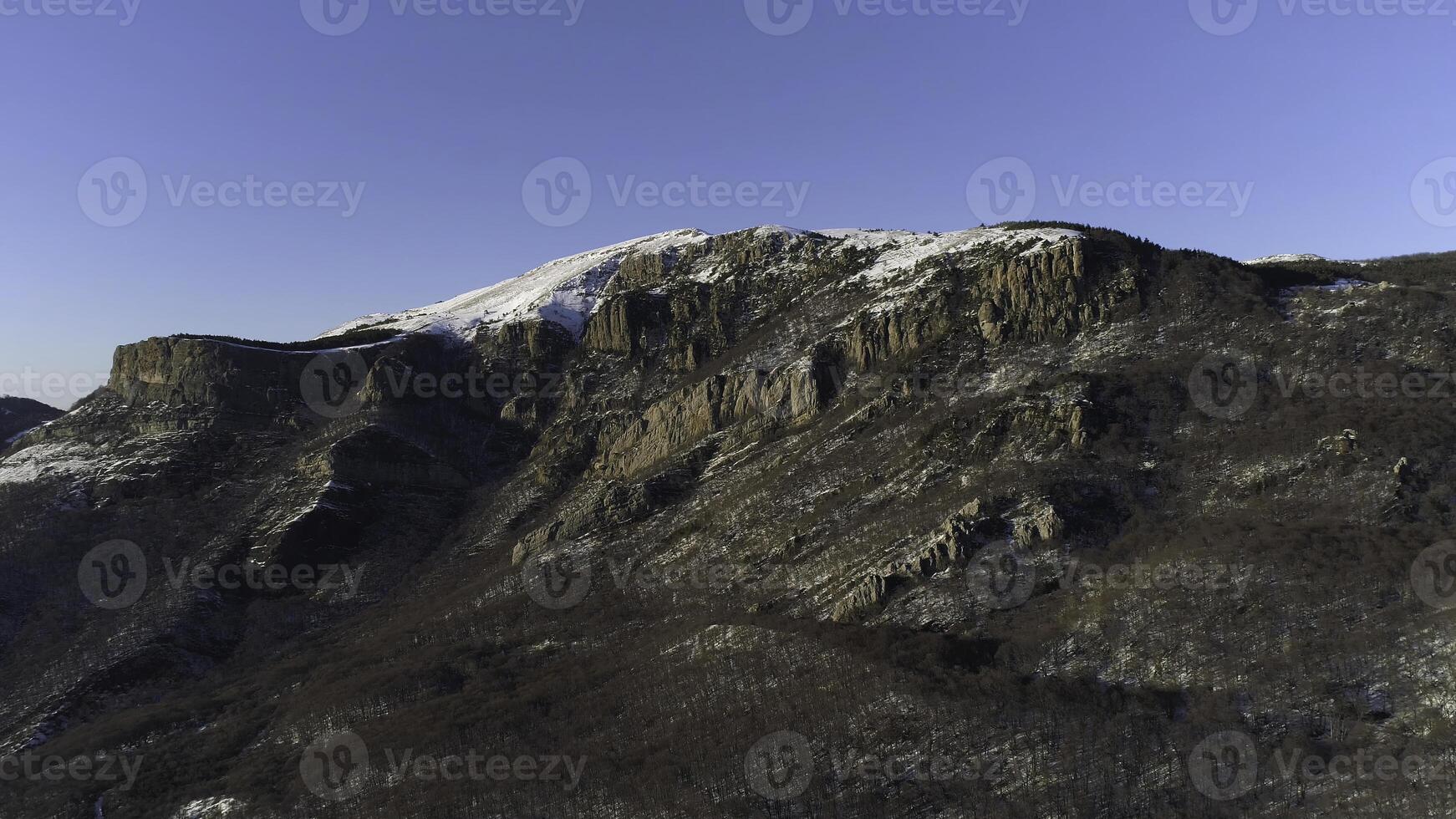 Aerial view of mountains on a sunny autumn day on blue clear sky background. Shot. Flying over snowy steep rocky walls with growing bald trees. photo