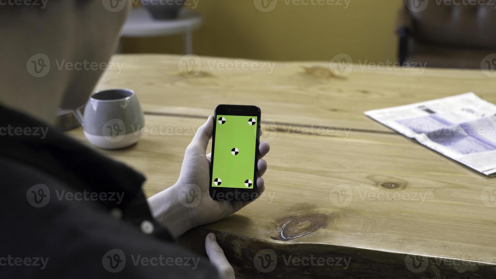 View over the shoulder of a businessman using the hand held cellphone with green screen touchpad on wooden table background. Stock footage. Man lloking at his device, chromakey. photo